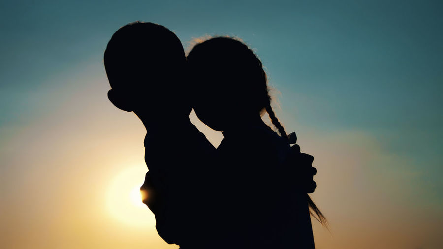 Silhouettes, figures of children, boy and girl, brother and sister hugging against the background