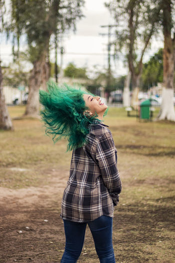 Cheerful woman tossing dyed green hair while standing on land