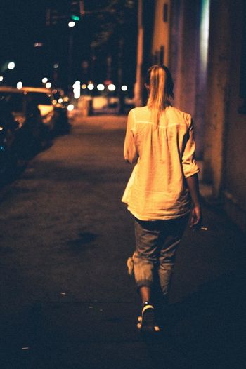 Rear view of woman walking on road at night