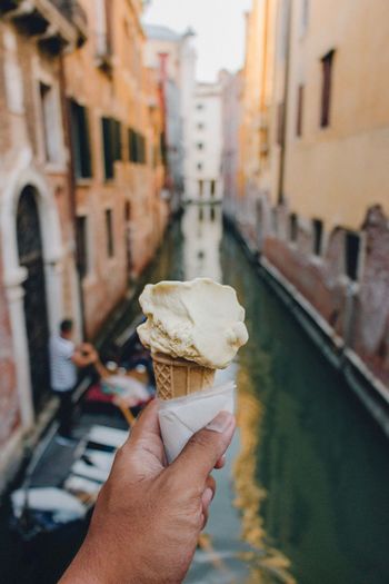 Close-up of hand holding ice cream cone against buildings