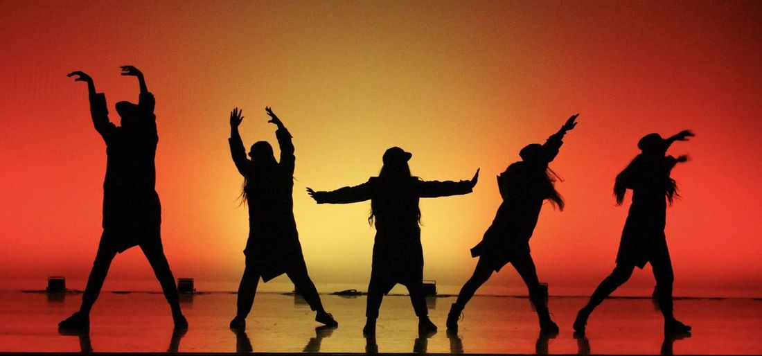 Silhouette people dancing against colored background