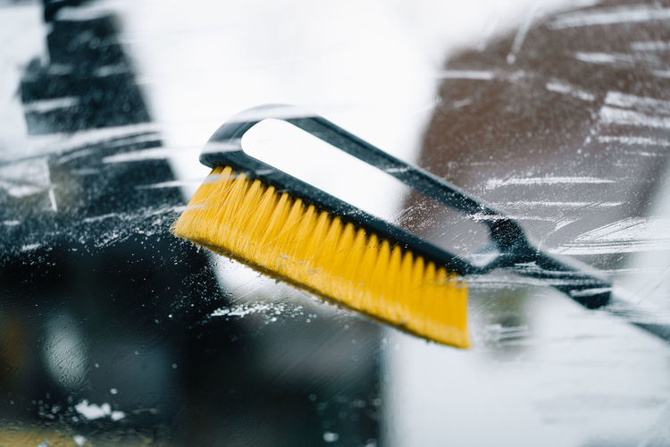 Close-up of yellow brush on wet frozen car windshield