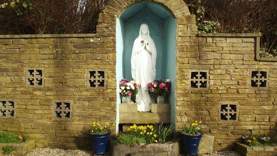 Virgin mary statue amidst colorful flowers