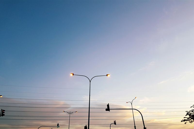 Low angle view of illuminated street light with electricity cables against sky during sunset