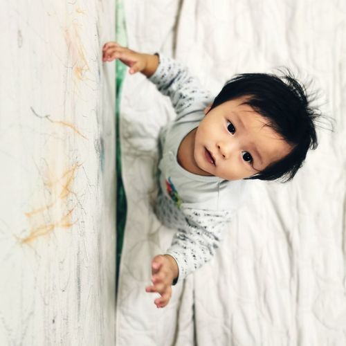 Portrait of cute baby lying on bed against wall
