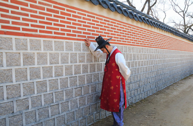 Side view of man in traditional clothing standing by wall