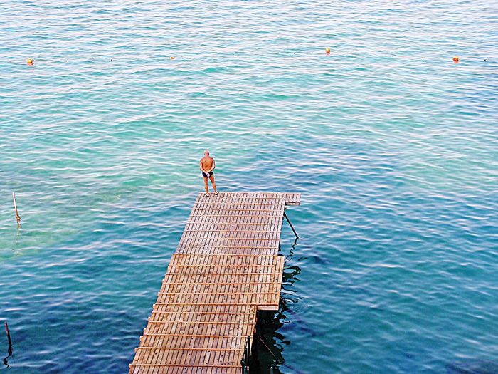 High angle view of shirtless senior man standing on jetty over sea