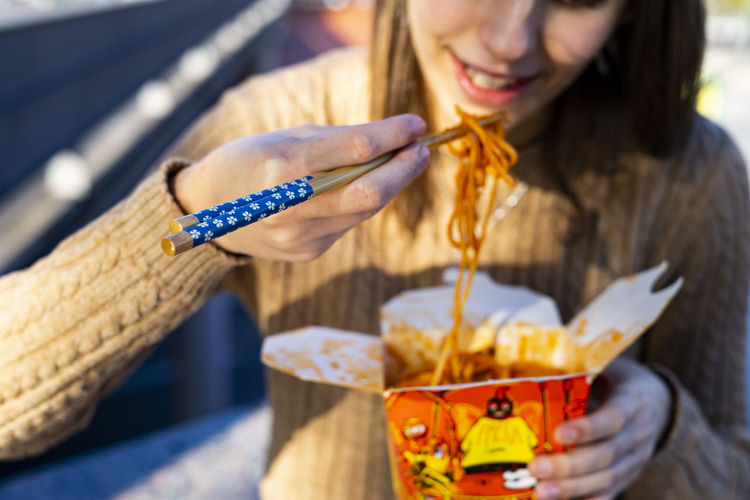 Girl eating chinese noodles with some blue chopsticks.