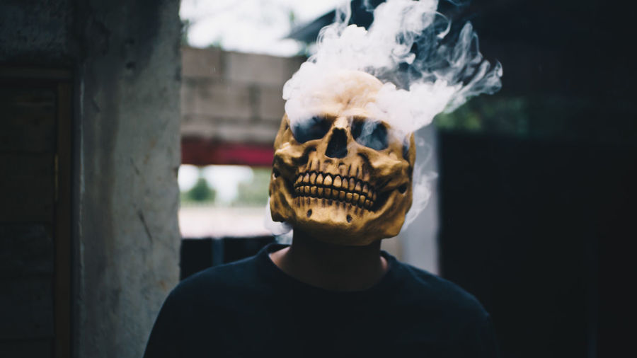 Close-up of man wearing skull mask with smoke emitting