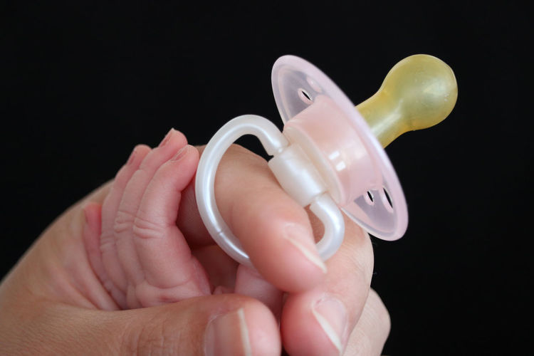 Close-up of image of hand holding pacifier against black background