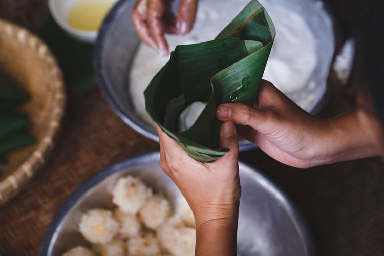 High angle view of woman wrapping rice cakes in banana leaf cone