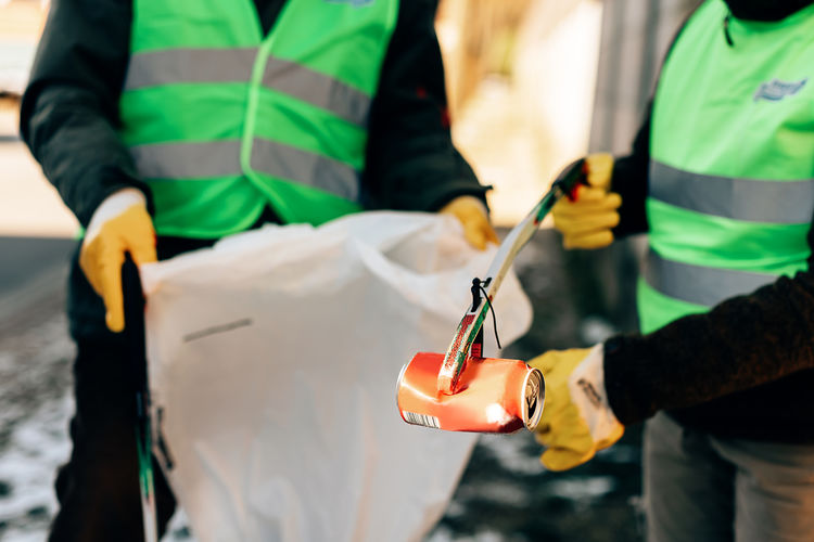 Volunteers with gloves and reflective vests collect cans thrown on the street. sustainability life. 