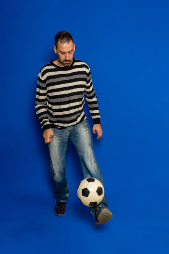 Full length of man playing with soccer ball over blue background