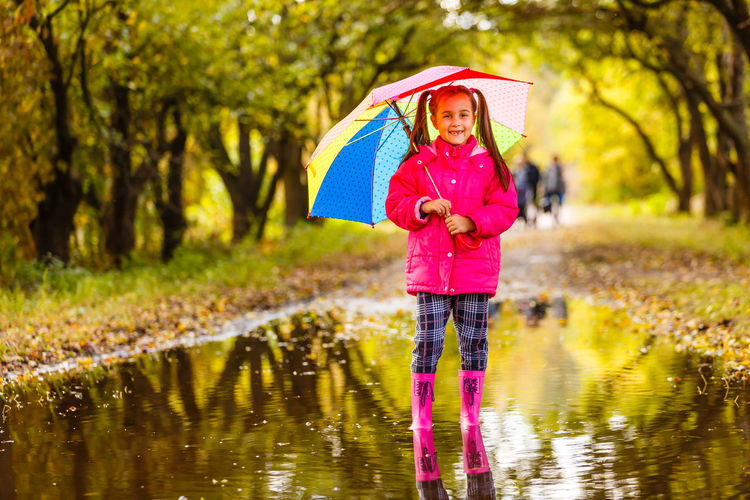 Full length of girl holding umbrella standing in lake during rainy season