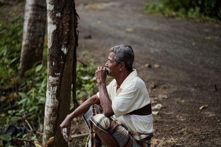Side view of senior man sitting and smoking cigarette on the side of the road