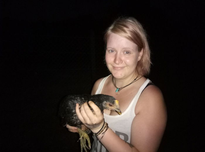 Portrait of young woman holding bird against black background