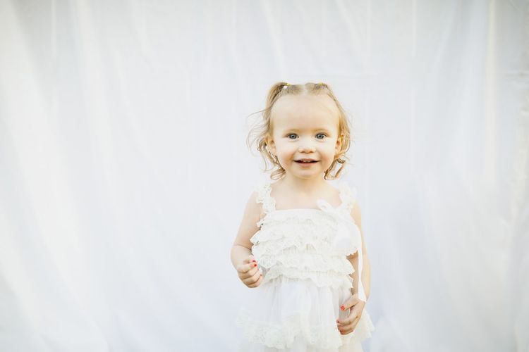 Portrait of cute girl standing against white curtain
