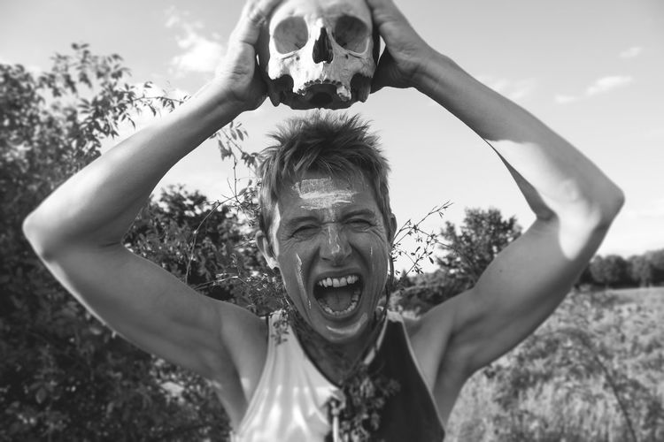 Mature man screaming while holding skull by plants