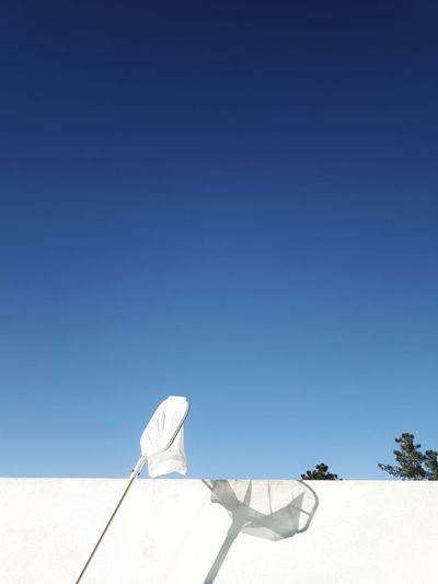 Low angle view of butterfly net by surrounding wall against clear blue sky
