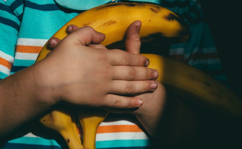 Midsection of child holding bananas