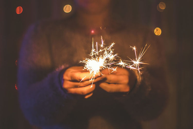 Midsection of woman holding lit sparkler at night