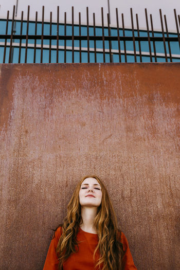 Redheaded beautiful woman leaning against a wall outdoors
