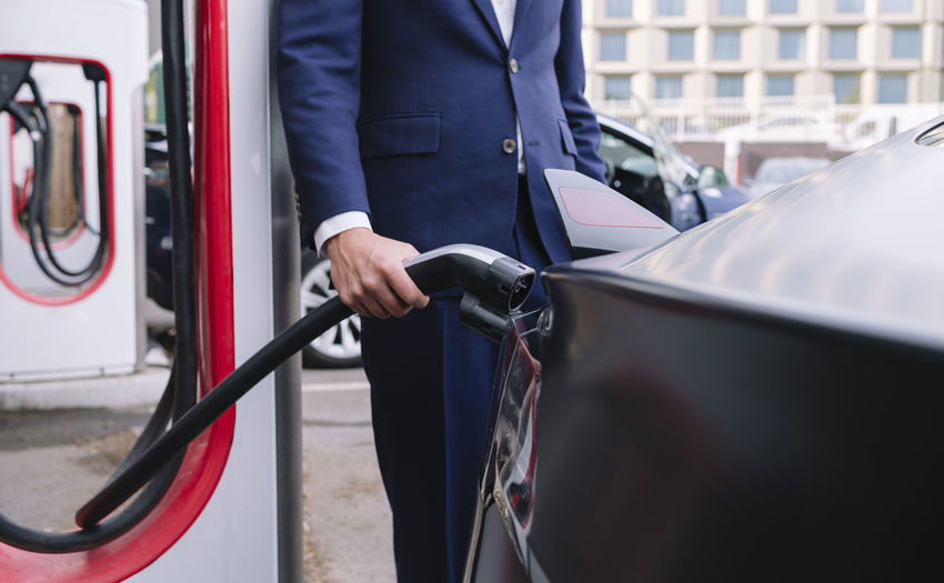 Businessman holding power cable charging car at station