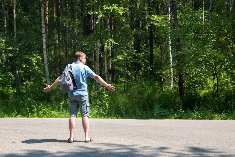 Male tourist auto stop spread his arms to the sides on an empty road.
