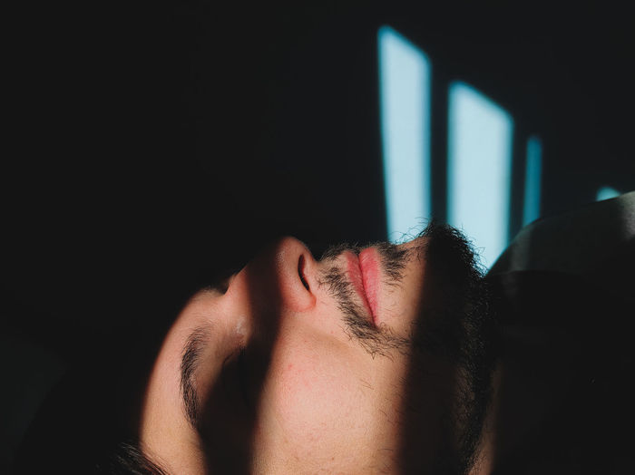 Close-up of man sleeping in darkroom with sunlight on face