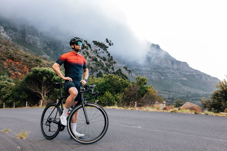 Rear view of man riding bicycle on road against mountain
