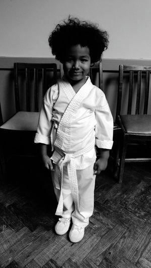 Portrait of boy in karate uniform standing by chairs