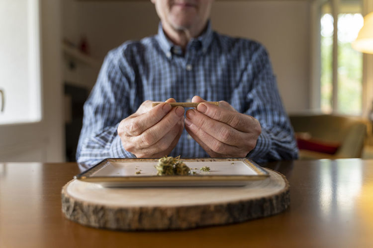 Senior man at home rolling marihuana joint
