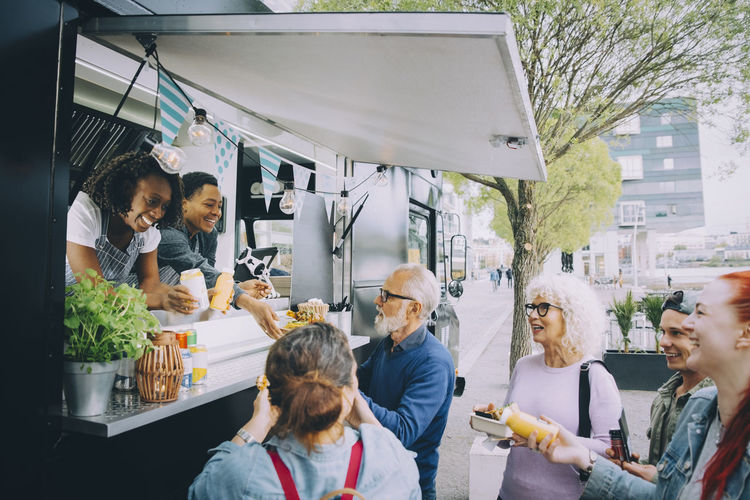 Smiling male and female customers talking to food truck owners in city