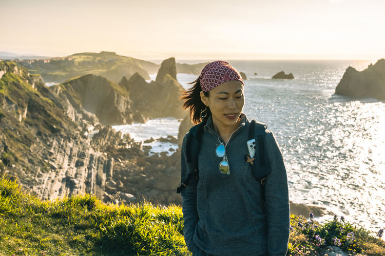 Asian female hiker smiling while standing on cliff against sea