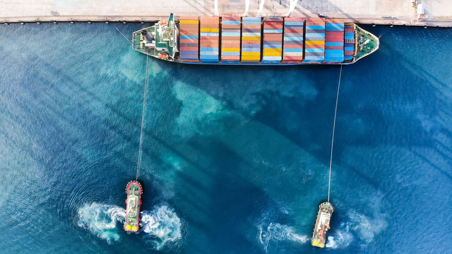 Aerial view of tugboats pulling container ship at harbor