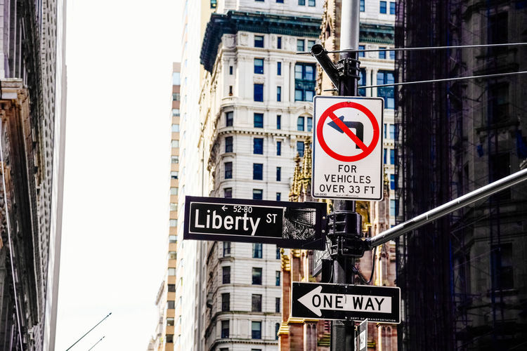 Road sign amidst buildings in city against clear sky