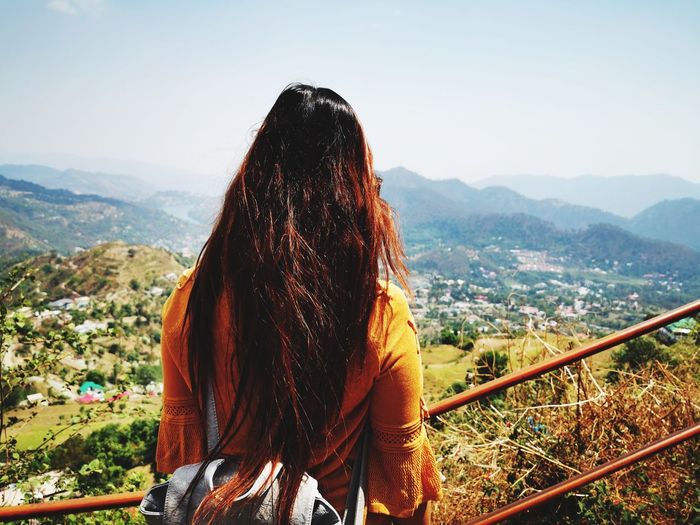 Rear view of woman standing by railing against cityscape and sky
