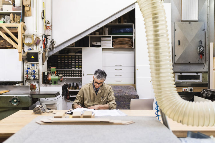 Male craftsperson writing while working at workshop