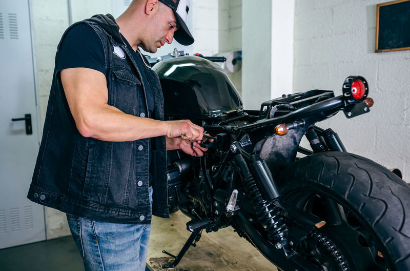 Side view of mature mechanic examining motorcycle in garage