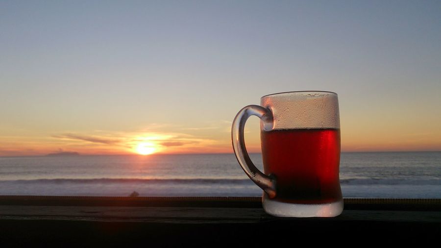 Close-up of beer on table against sea during sunset