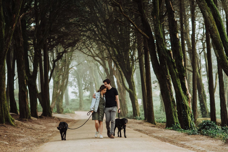 Couple embracing while walking dogs on a leash down a road in forest