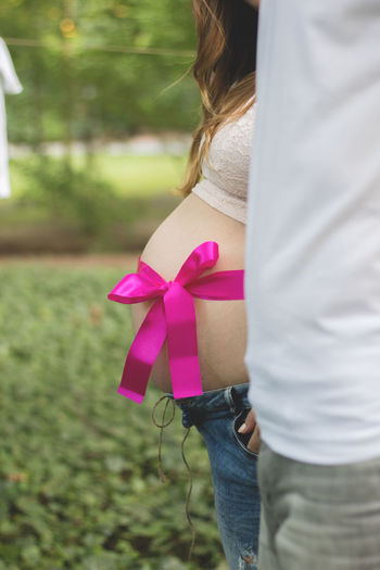 Midsection of pregnant woman with man standing on grassy field at park