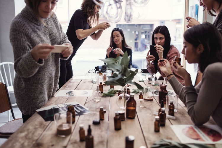 Multi-ethnic female coworkers photographing perfumes on table at workshop