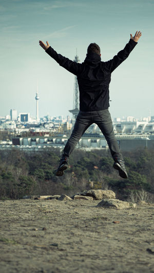 Rear view of man with arms raised jumping on land against sky