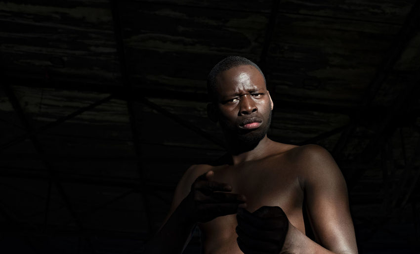 Portrait of confident shirtless man standing against black background