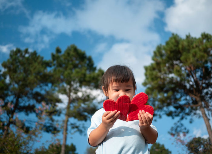 Girl holding heart shapes against trees
