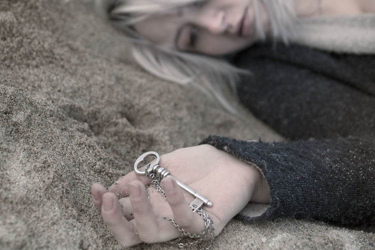 Close-up of thoughtful young woman holding key pendant while lying on sand