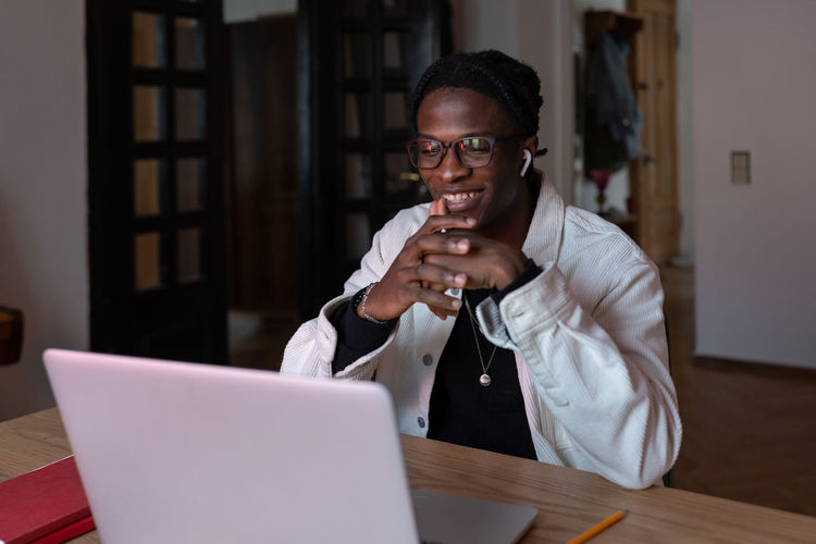 Young smiling happy african man remote worker in eyewear looking at laptop screen reading e-mail