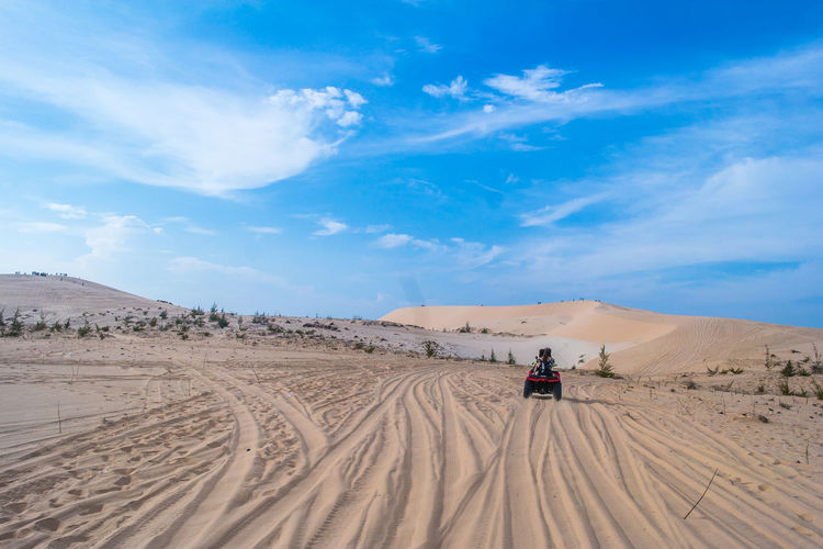 Rear view of people riding quadbike at desert against sky