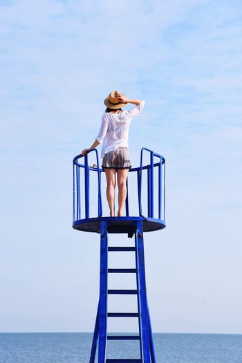 Rear view of woman standing on lookout tower looking at sea against sky
